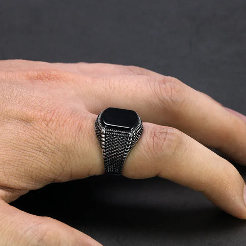 Image of Hand wearing a silver ring with a black stone on a dark background