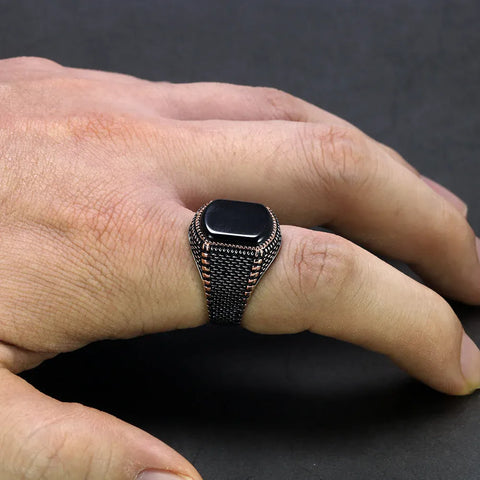 Image of Hand wearing a black ring with intricate design on a dark background