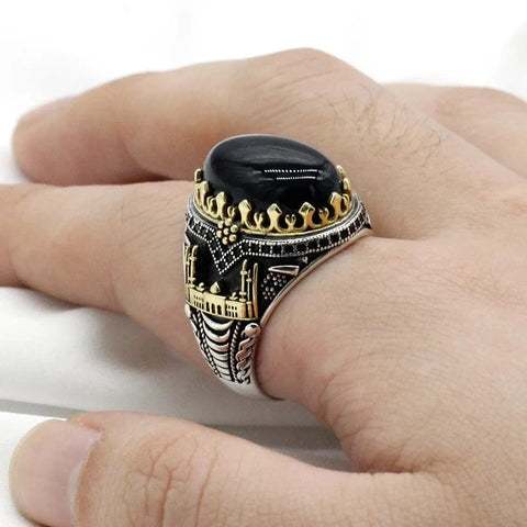 Image of Decorative ring with black stone and gold accents on a finger against a white background