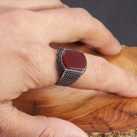 Image of Close-up of a hand wearing a silver ring with a red stone on a wooden surface.