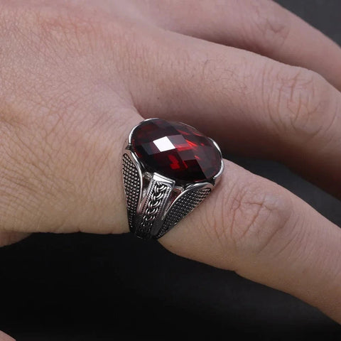 Image of Silver ring with a red gemstone on a finger against a dark background