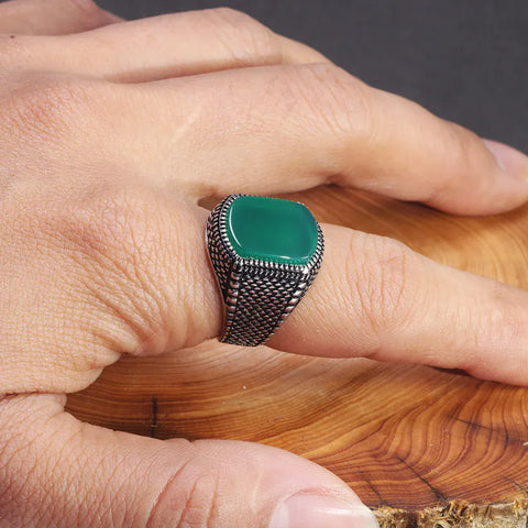 Image of Hand wearing a silver ring with a green stone on a wooden surface