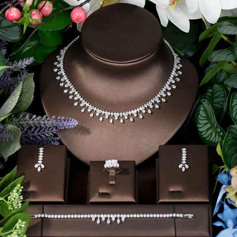 Image of Jewelry set including necklace, earrings, and ring on a brown stand with greenery around.